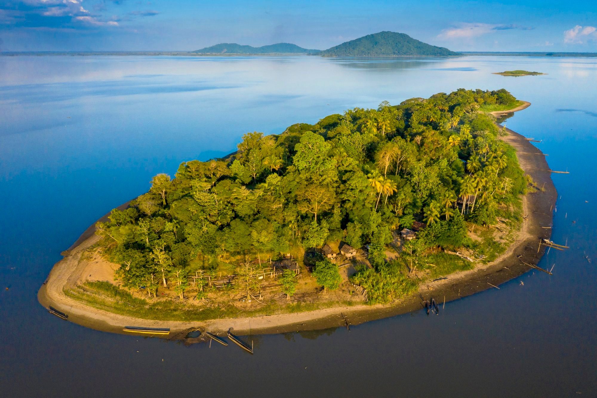 Aerial view of a small forested island with dugout canoes on a calm lake