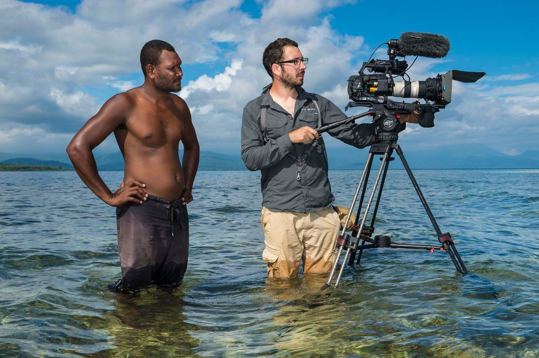 Cameraman filming a local man standing in the sea, Papua New Guinea