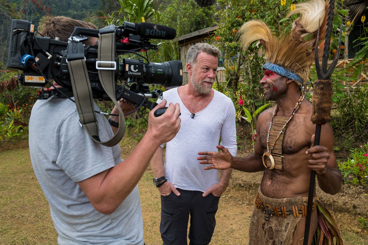 Cameraman filming a presenter talking with a Huli man in ceremonial dress