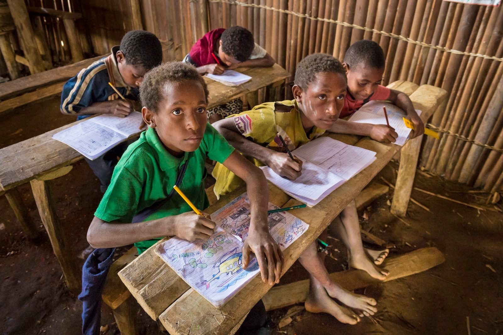 Children writing at wooden desks in a bush-material school in Papua New Guinea