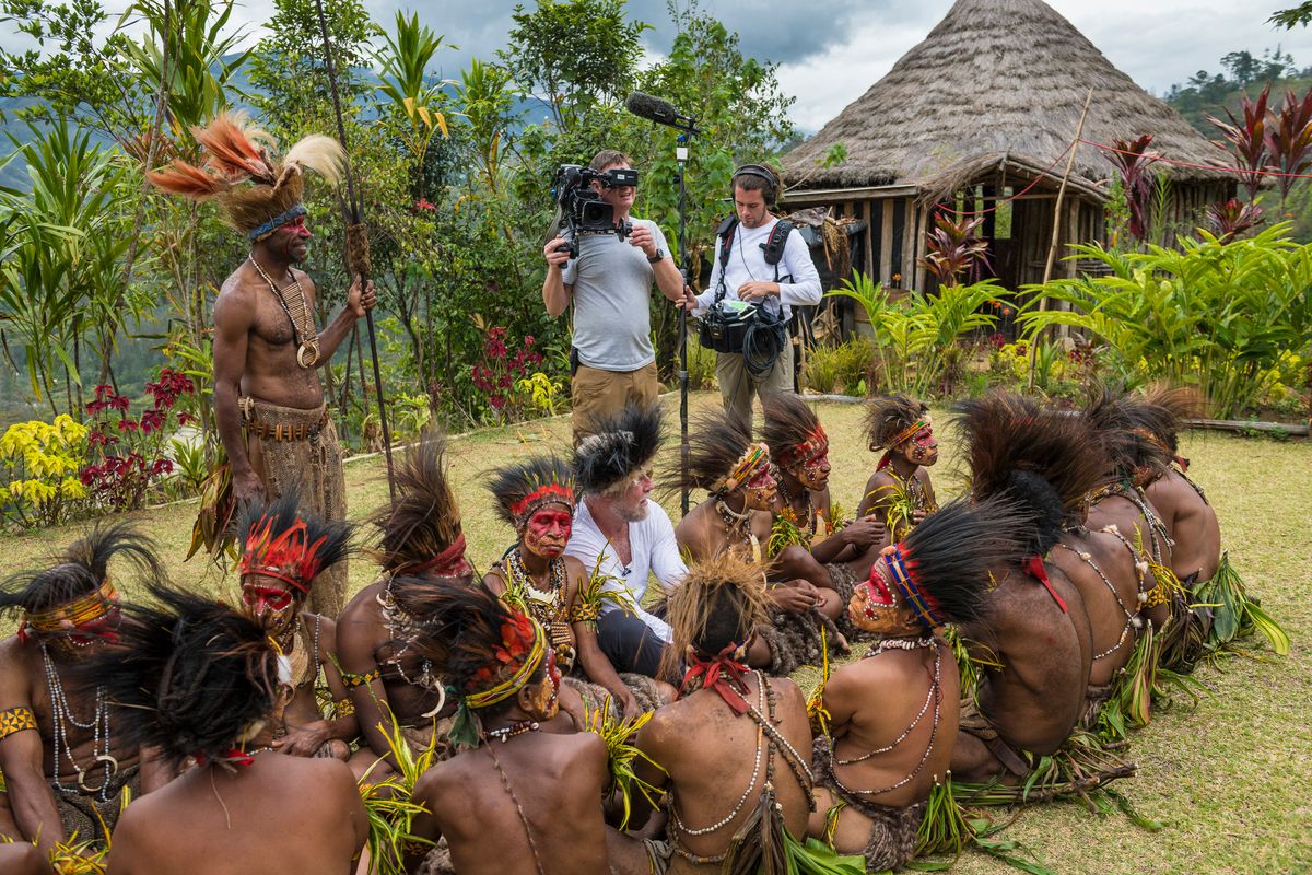 Camera and sound crew filming a presenter sitting among Huli women in ceremonial paint