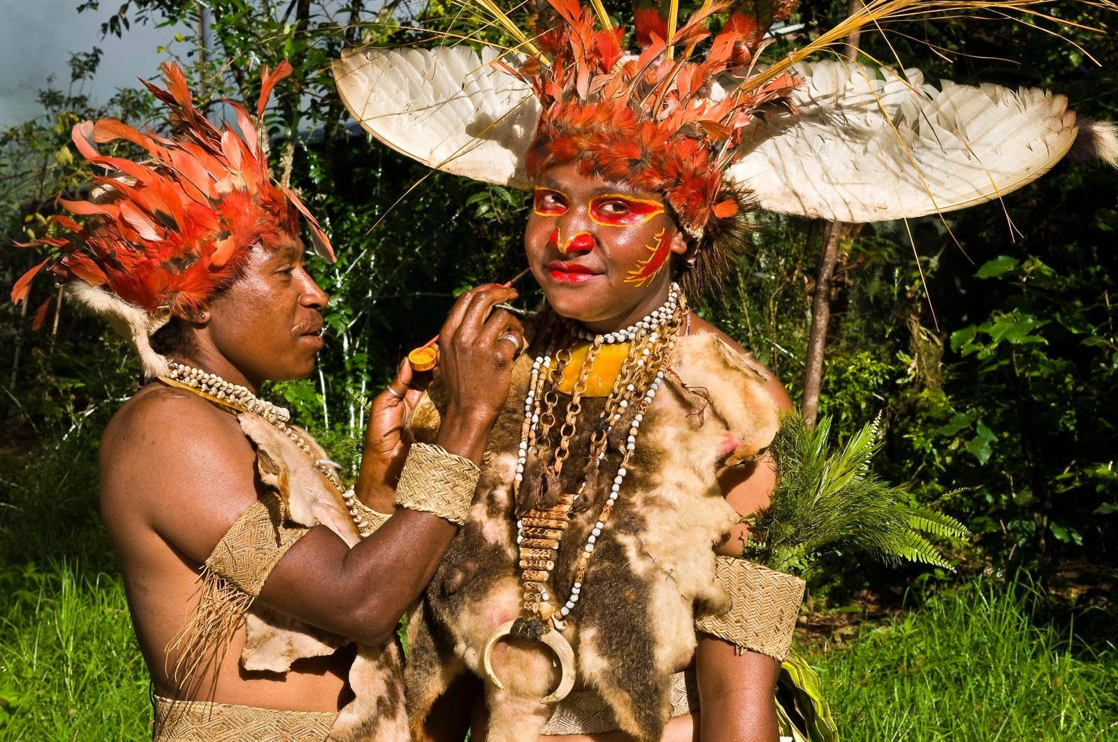 Highlands man painting the face of a woman in feather headdress before a sing-sing