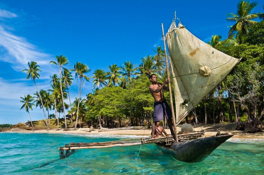 Man sailing an outrigger canoe off a tropical beach