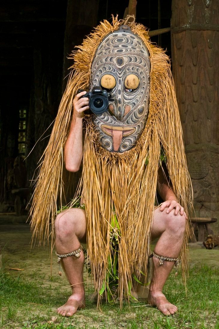 Marc Dozier, camera in hand, wearing a traditional mask and grass costume