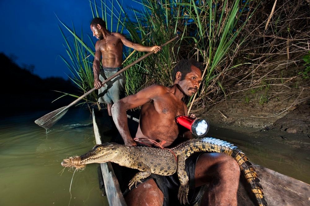 Men with a crocodile in a dugout canoe at dusk
