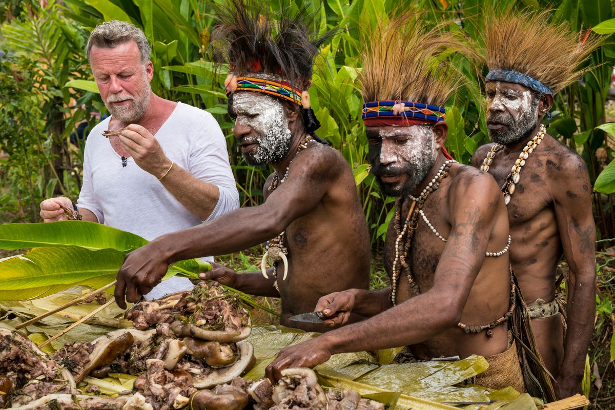 Presenter tasting food from a mumu earth-oven feast with Highlands men