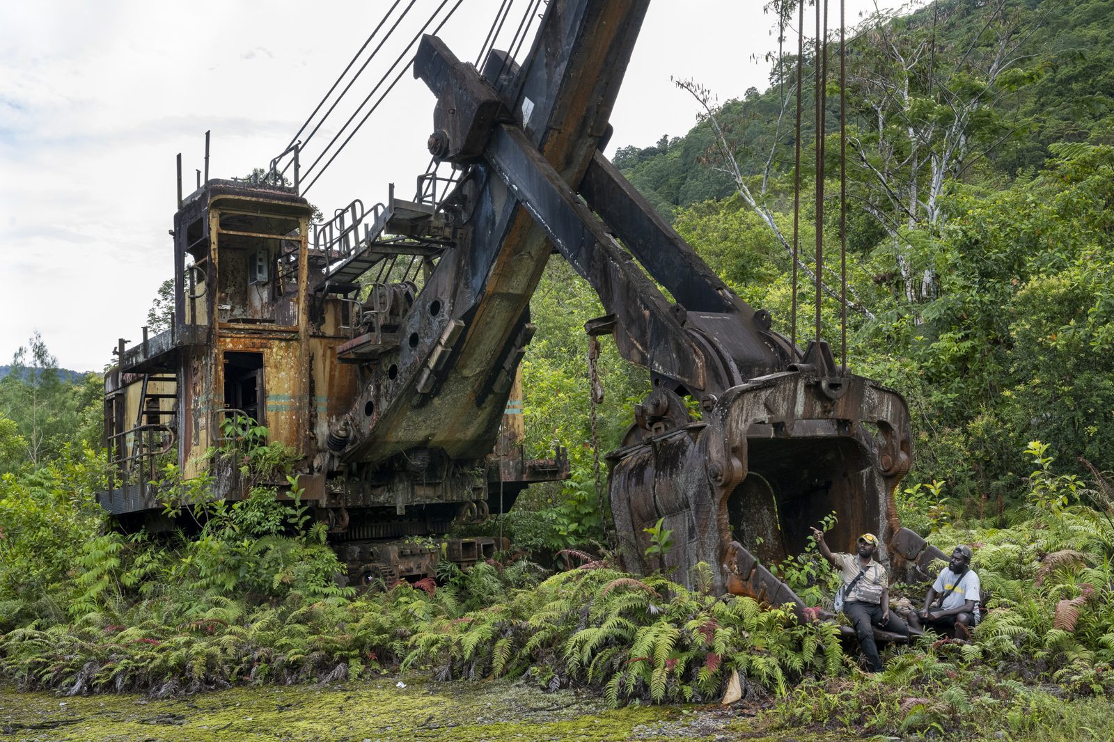 Rusting mining shovel overgrown by rainforest at Panguna, Bougainville