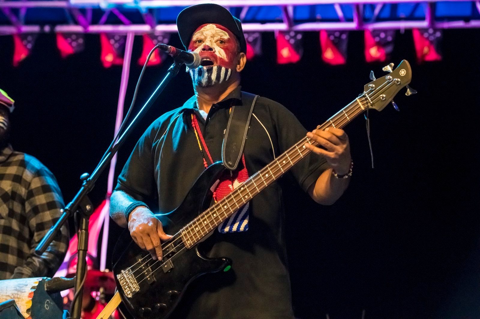 Singer with a painted face playing bass guitar on stage