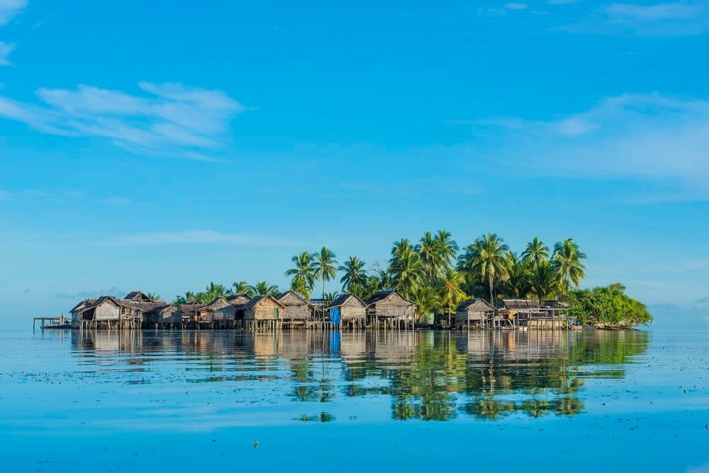 Stilt village on a small island reflected in a calm lagoon